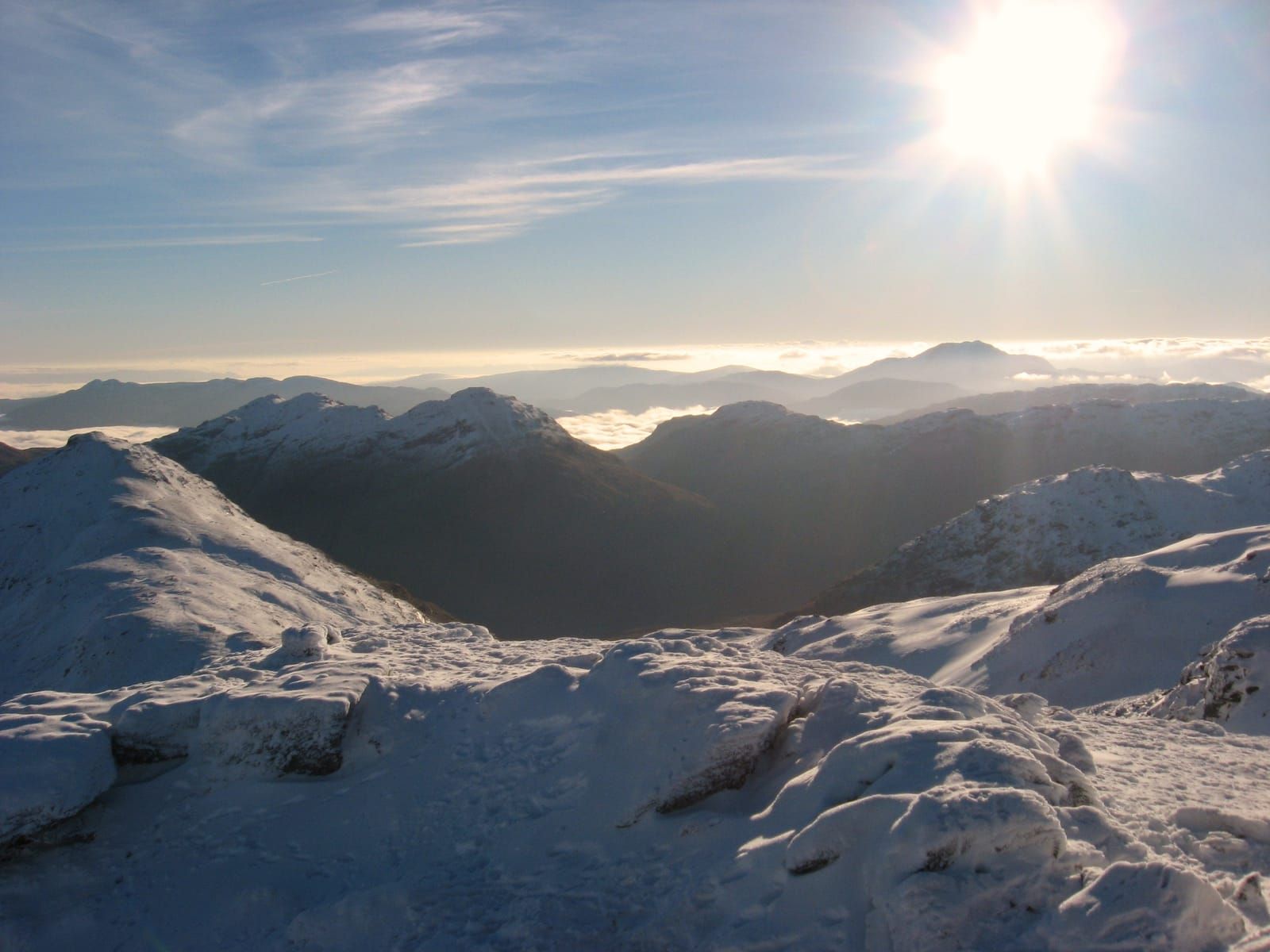 Brilliant sun on brilliant white peaks in the view from the frozen summit of Beinn Tulaichean